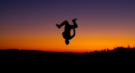 A dynamic silhouette of a figure performing a backflip against a colorful sunset, with vibrant orange and purple