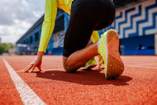 Sprinter at the starting line, ready to race on an outdoor track, wearing bright sportswear and spiked running shoes, captured from a low angle