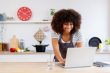 Happy chef using laptop in modern kitchen, searching online recipes and cooking classes, enjoying...