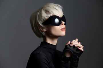Fashionable young woman with short blonde hair and oversized sunglasses, wearing a black top, posing elegantly. Modern and stylish concept of beauty.