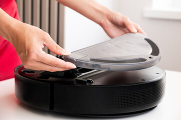 woman cleaning and installing water container in robot vacuum cleaner. housewife in red dress preparing vacuum cleaner before cleaning or cleaning it from dust and debris after cleaning house
