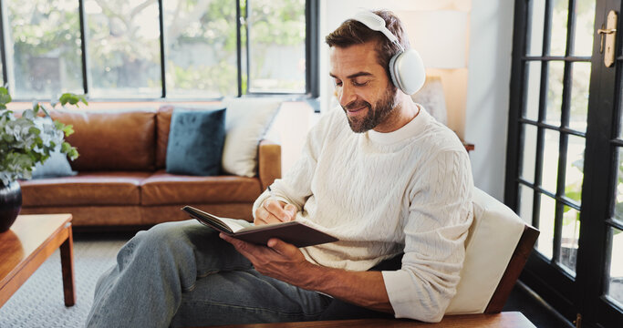 Home, man and smile with headphones for notebook, writing thoughts and personal reflection with music. Sofa, male person and happiness with audio track for journal, diary or to do list in living room