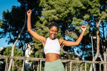 Happy athlete celebrating victory in a park raising her arms