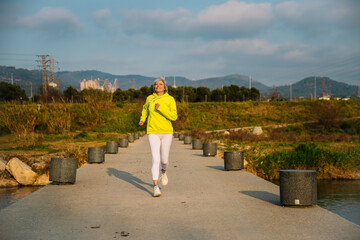 Senior woman running in a park by the river, maintaining health and wellness