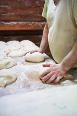 Baker forming dough into loaves on wooden floured table