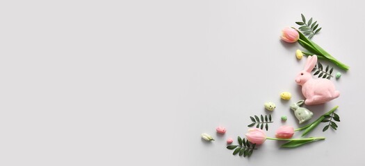 Easter eggs, green leaves, flowers and decorative bunnies on light background with space for text