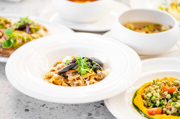 A close-up of gourmet dishes on a table, featuring colorful pasta with mussels, vibrant vegetables, and soup. Perfect for food, culinary, or dining themes.