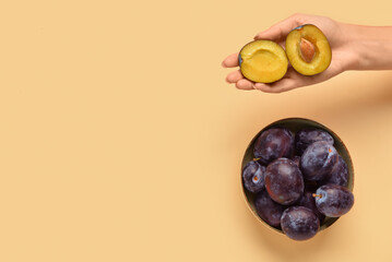 Woman holding halves of fresh plum on yellow background