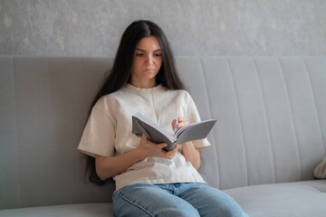 A woman with long hair is deeply focused on reading a book indoors, surrounded by a calm and...