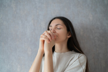 A woman sits peacefully, eyes closed and hands clasped in prayer, reflecting on her thoughts in a calming indoor environment.