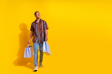Fototapeta premium Young man carrying shopping bags on vibrant yellow background expressing happiness and style