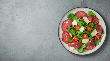 Salad featuring beef carpaccio, spinach, cherry tomatoes, and parmesan on a white plate against gray background Healthy eating