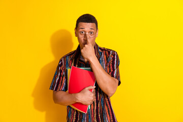 Young man with stylish glasses holding a red folder, wearing a colorful casual shirt posing against...