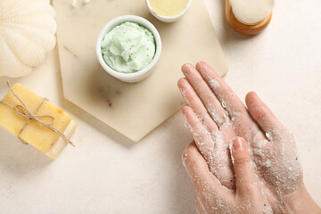 Woman applying scrub onto hands on light background, closeup