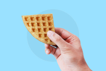 Hand Holding a Golden Waffle Slice on Vibrant Blue Background – Perfect for Food Advertisements and Social Media Promotions