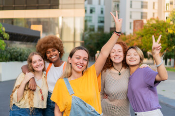 Joyful group of diverse young women celebrating friendship with playful poses and cheerful expressions in a vibrant outdoor setting filled with laughter and happiness