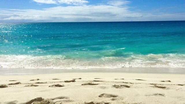 A serene white sandy beach with gentle waves lapping at the shore under a clear blue sky. Tropical atmosphere 