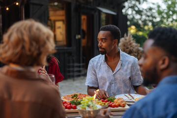 A man in a shirt sitting with his friends at a backyard dinner party