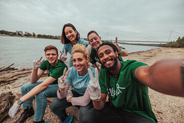 Five volunteers in uniforms sitting by the river taking a selfie after cleaning the shore