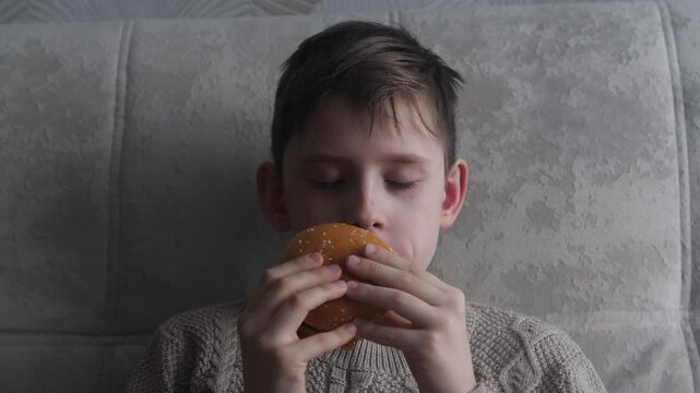 portrait of a Caucasian handsome boy 11 years old with pleasure eating an appetizing burger while inside, the child eats fast food with pleasure