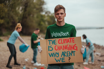 Volunteer holding protest sign about climate change during river cleanup with group of people