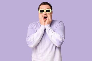 Shocked young man in glasses on lilac background