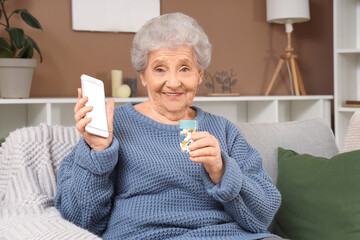 Senior woman taking pill bottle and mobile phone sitting on sofa at home