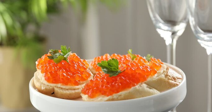 Tasty sandwiches with red caviar on spinning plate against blurred background, closeup