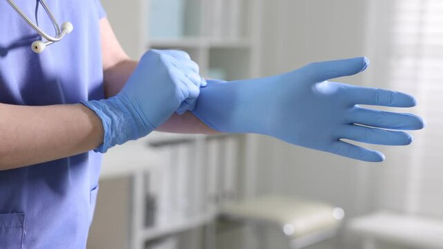 Medical worker putting on gloves in hospital, closeup