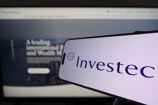 Kiel, SH, Germany March 24 2025: Smartphone displaying Investec logo in front of company website on a monitor, illustrating modern digital communication in business environments