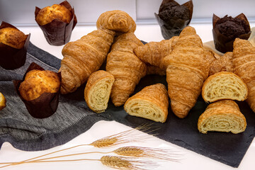 Fresh crispy croissants and muffins on table in cafe, top view. Fresh various pastries in bakery showcase.