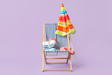 Striped deck chair with colorful umbrella, handbag and traveller pillow on lilac background
