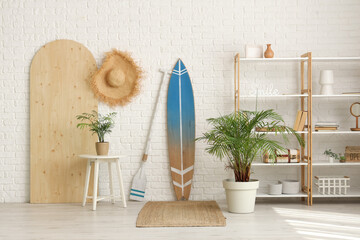 Interior of modern stylish room with surfboard and shelving unit near white brick wall