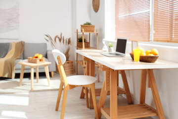 Laptop and wicker basket with citruses on workplace in white living room, blurred view
