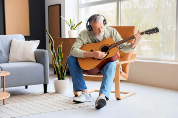 Mature man in headphones playing guitar at home