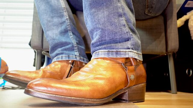 Low angle closeup on man's feet in brown leather shoes, moving it like he is nervous or tense