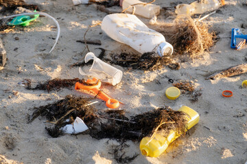 Scattered plastic bottles, broken containers, and tangled fishing nets pollute sandy shore. Ocean waves bring environmental waste, raising awareness urgent ecological issues marine conservation effort
