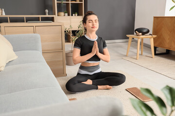 Fototapeta premium Sporty young woman with Sadhu board meditating on floor at home