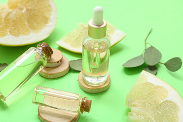 Bottles of cosmetic oil, green leaves and pieces of fresh pomelo on green background, closeup