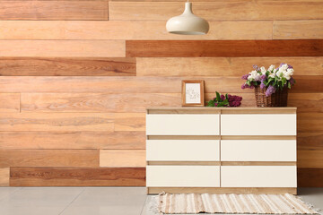 Stylish wooden cabinet and vase with flowers in room