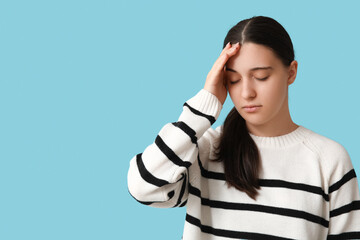 Beautiful young woman suffering from headache on blue background