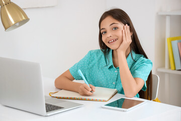 Little schoolgirl studying online at table in bedroom