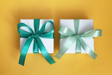 Flat lay on two elegant gift boxes tied with emerald green ribbons on a bright yellow table.