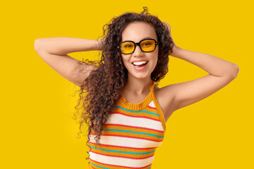 Beautiful African-American woman with sunglasses on yellow background