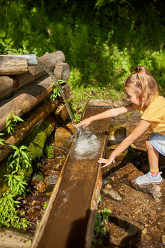 Child refreshing face at natural spring during sunny day in peaceful forest setting