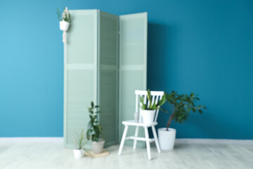 Blurred view of living room with folding screen, chair and different houseplants near blue wall