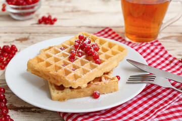 Plate of sweet Belgian waffles with fresh red currants and glass cup of tea on white wooden background