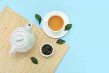 Cup and teapot of hot tea with dried leaves on blue background
