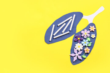 Paper lungs with plasticine flowers and cigarettes on yellow background