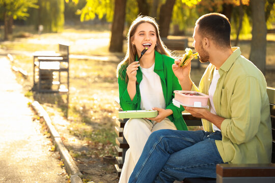 Young couple having lunch on bench in park